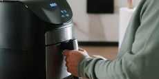 A person using an air fryer appliance in a kitchen. A person using an air fryer appliance in a kitchen.