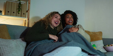 Two smiling women watch TV at home in the evening with dim lighting. Two smiling women watch TV at home in the evening with dim lighting.