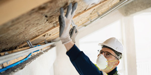 A professional worker in protective gear installing insulation in a residential building's attic. A professional worker in protective gear installing insulation in a residential building's attic.