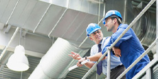 Workers discussing inside industrial facility with visible ducts and pipes. Workers discussing inside industrial facility with visible ducts and pipes.