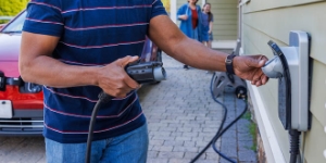 A man plugs an electric charger. The background shows his interracial family walking around and approaching. A man plugs an electric charger. The background shows his interracial family walking around and approaching.