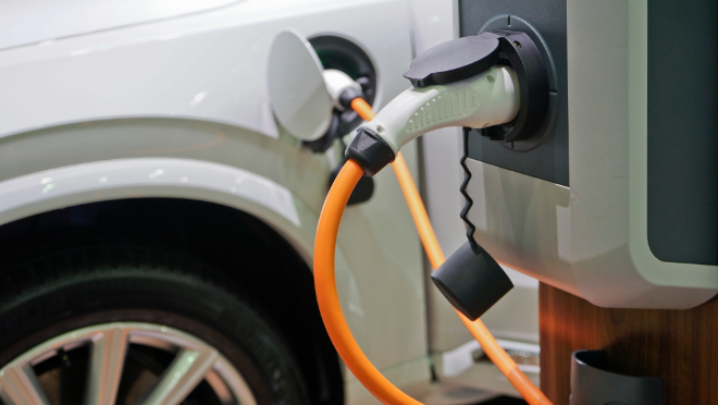 An electric vehicle is plugged in at a charging station in a parking lot.