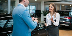 Sales manager holding car charging adapter and explaining the features of an electric car in showroom.