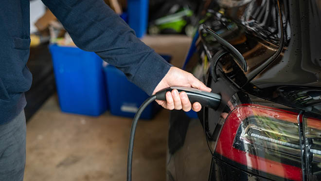 A side view close up shot of a person plugging cable in electric car.