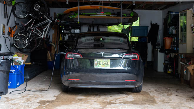 A black Tesla EV charging inside a home garage.