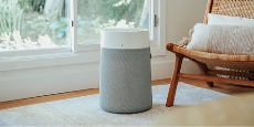 A portable air purifier in a room with the lower portion of a large window in the background on the left and on the right part of a brown wicker chair with white cushions. A portable air purifier in a room with the lower portion of a large window in the background on the left and on the right part of a brown wicker chair with white cushions.